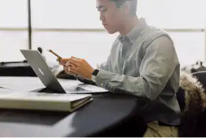 Man looking at phone and working from laptop